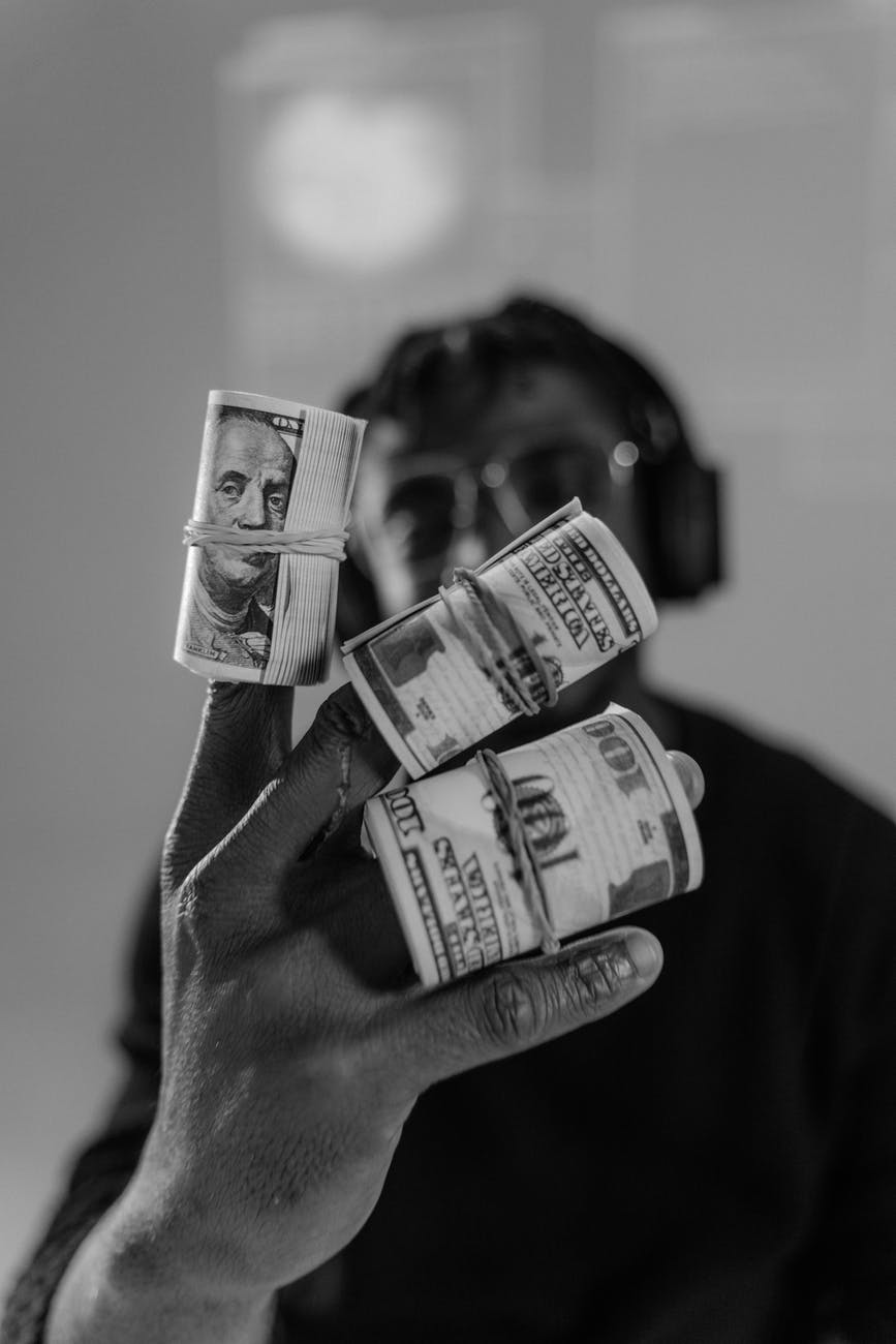 grayscale photograph of rolls of money on a person s fingers